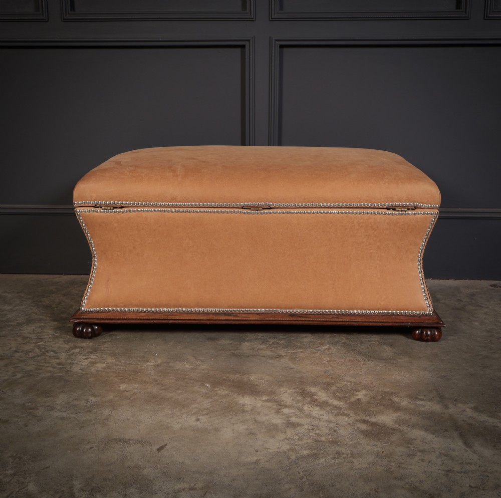 A rectangular tan leather upholstered box ottoman featuring brass stud trim and concave sides on a dark rosewood plinth base with turned feet. View XIII