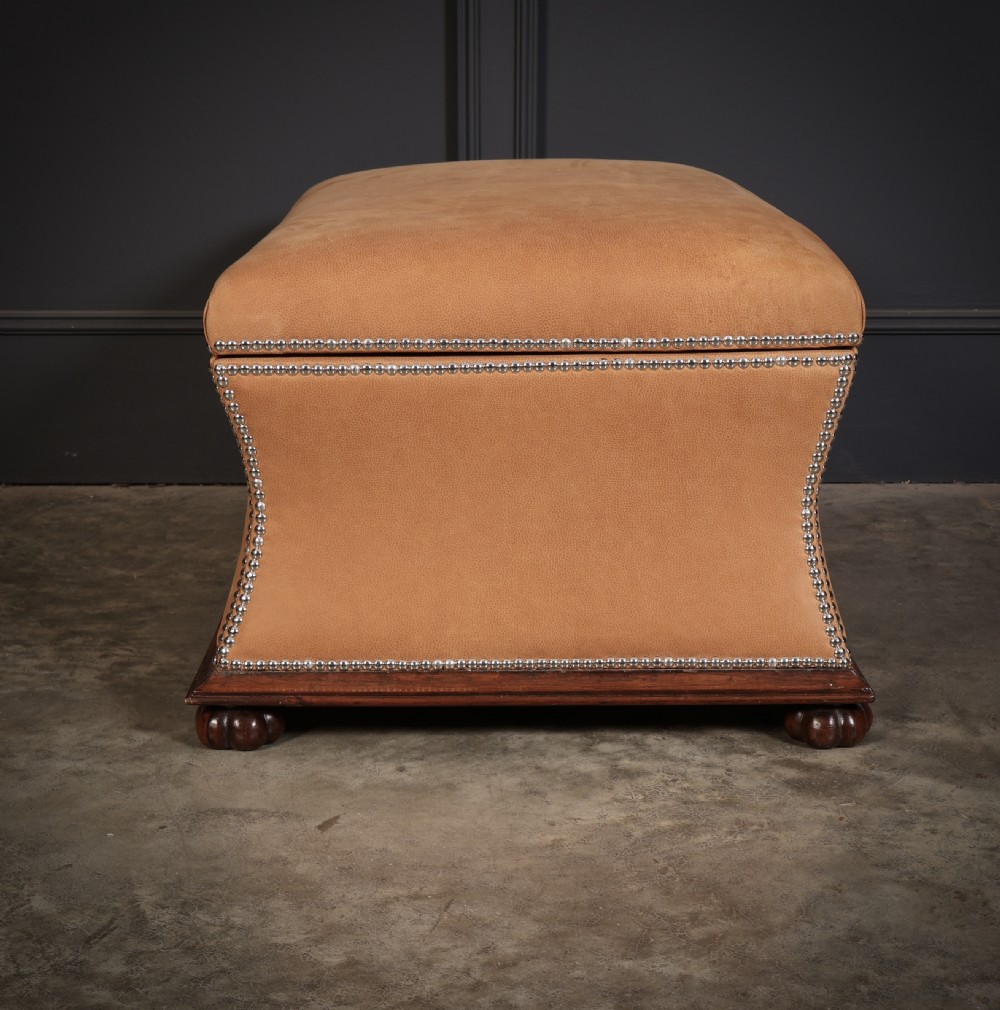 A rectangular tan leather upholstered box ottoman featuring brass stud trim and concave sides on a dark rosewood plinth base with turned feet. View XIV