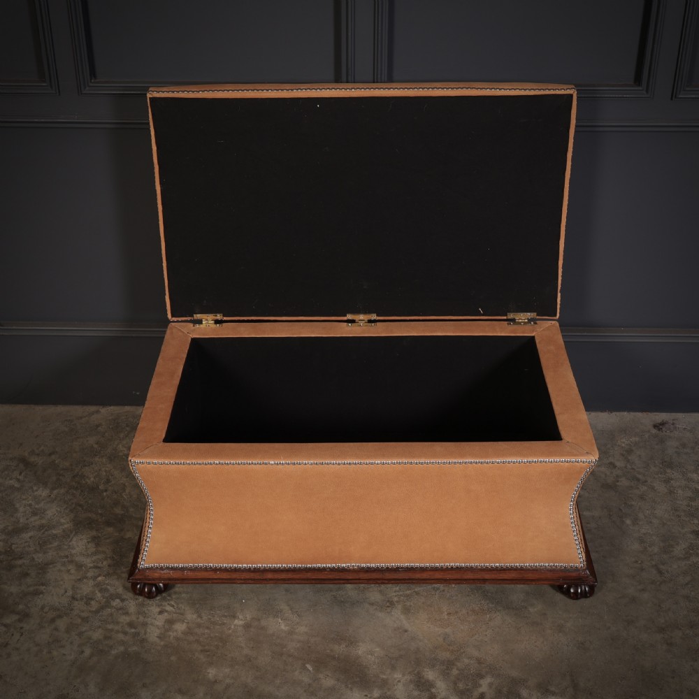 A rectangular tan leather upholstered box ottoman featuring brass stud trim and concave sides on a dark rosewood plinth base with turned feet. View XV