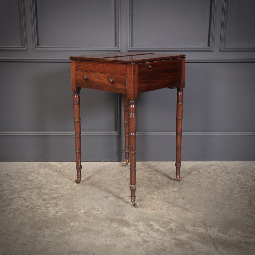 An antique Regency mahogany writing table featuring an adjustable leather-lined ratcheted reading slope, drop side flaps, a single drawer, and ring-turned legs with brass castors. View IV