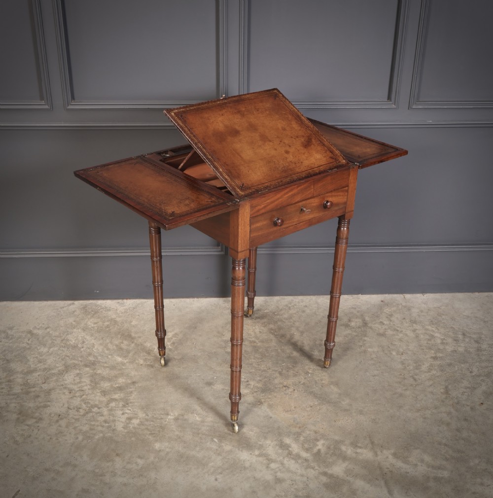 An antique Regency mahogany writing table featuring an adjustable leather-lined ratcheted reading slope, drop side flaps, a single drawer, and ring-turned legs with brass castors.