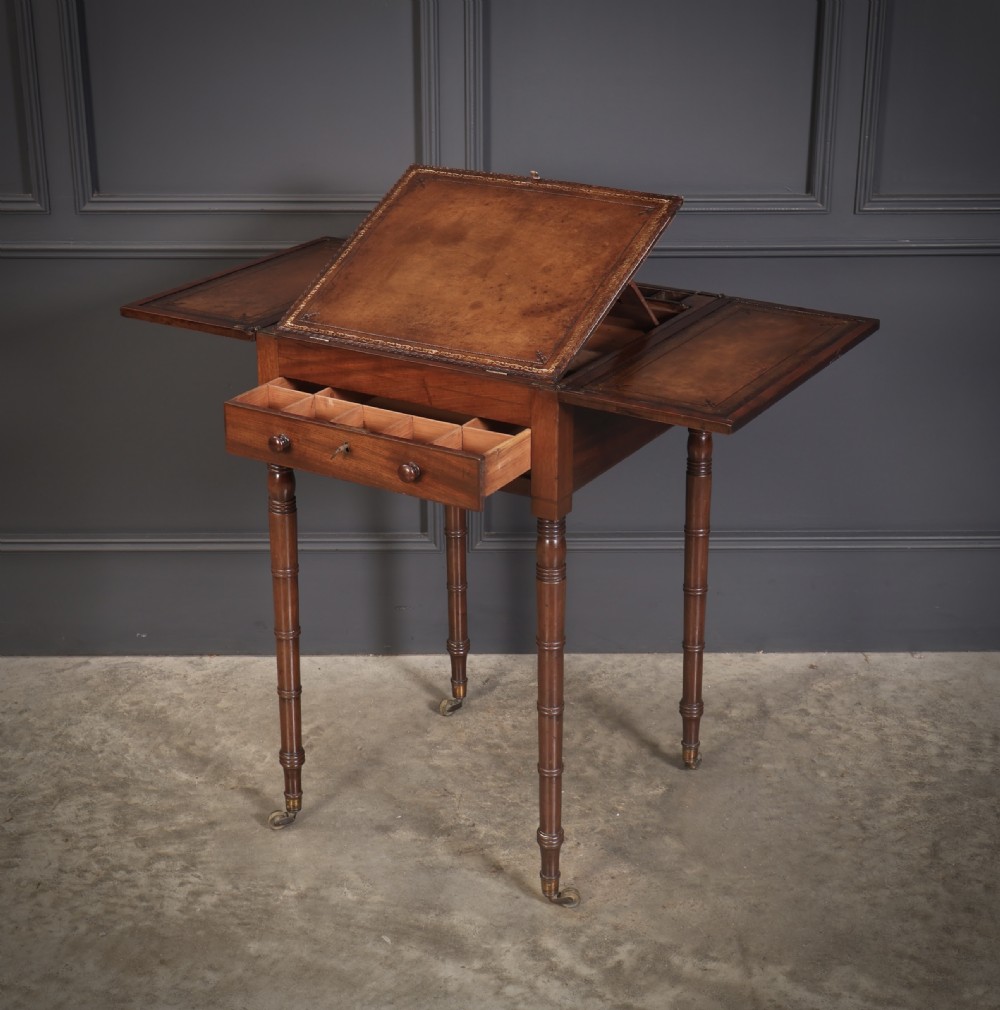 An antique Regency mahogany writing table featuring an adjustable leather-lined ratcheted reading slope, drop side flaps, a single drawer, and ring-turned legs with brass castors. View XV