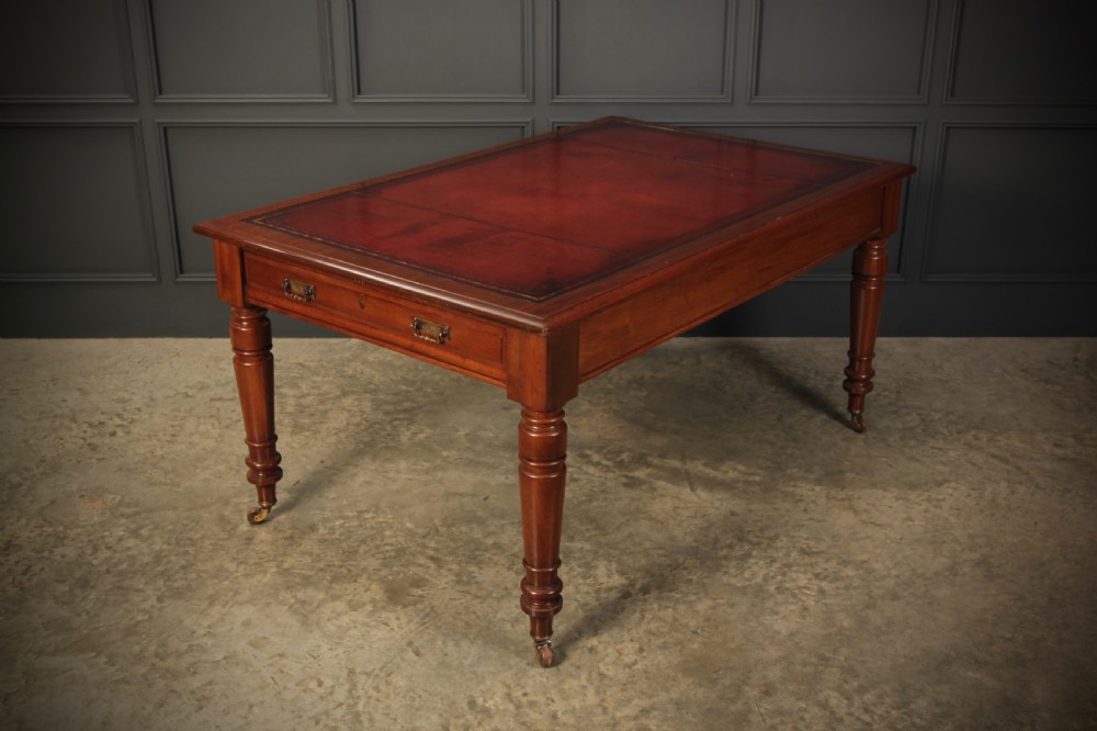 A Victorian mahogany writing table with a red leather inset surface, turned legs, and brass castors. View V