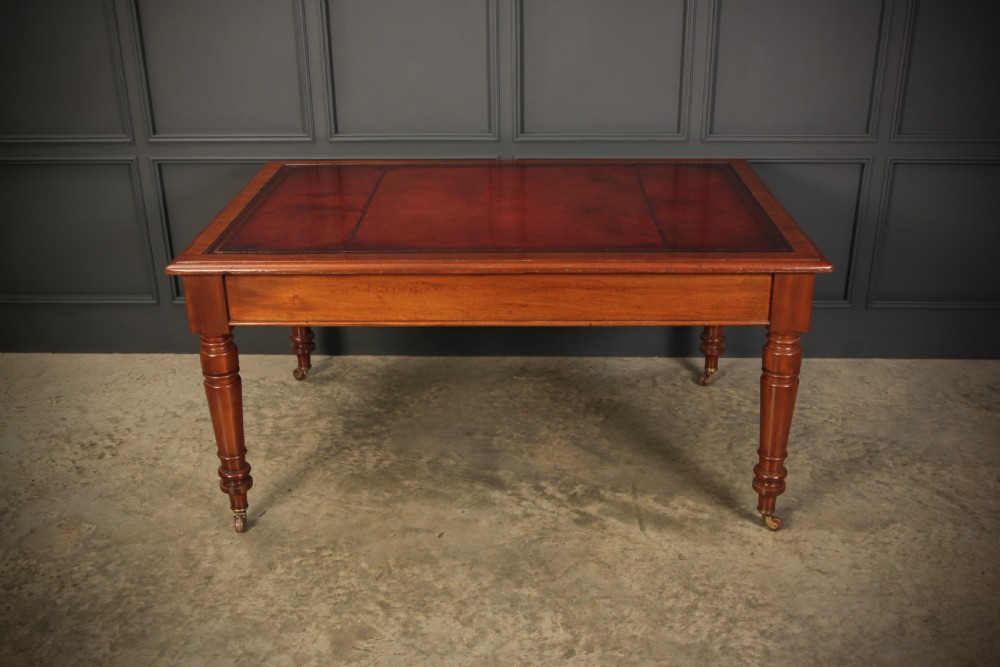 A Victorian mahogany writing table with a red leather inset surface, turned legs, and brass castors. View II