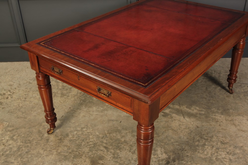 A Victorian mahogany writing table with a red leather inset surface, turned legs, and brass castors. View IV