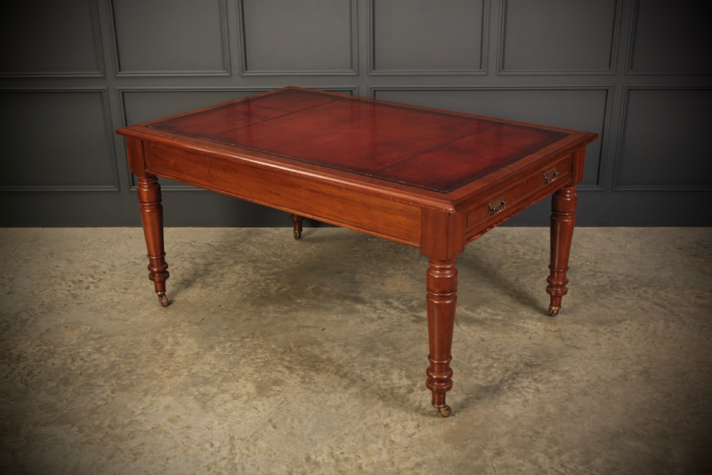 A Victorian mahogany writing table with a red leather inset surface, turned legs, and brass castors.