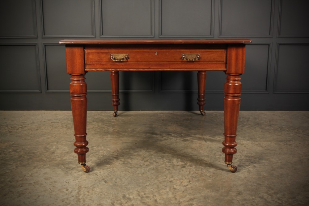 A Victorian mahogany writing table with a red leather inset surface, turned legs, and brass castors. View VII