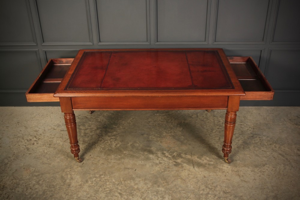A Victorian mahogany writing table with a red leather inset surface, turned legs, and brass castors. View VIII