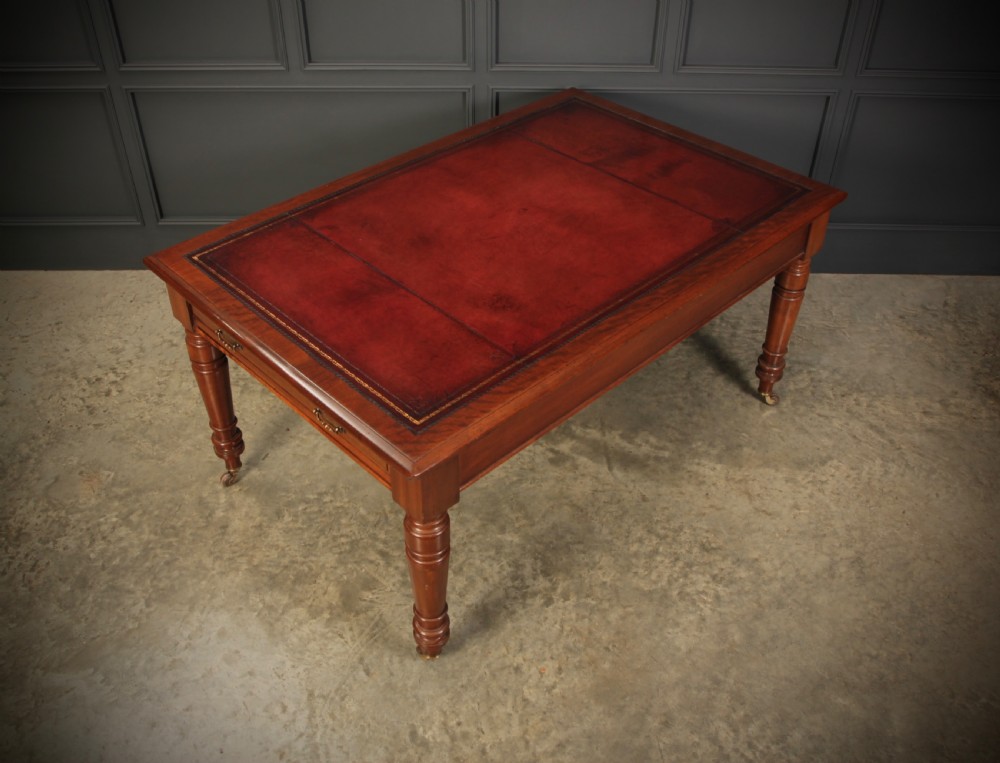 A Victorian mahogany writing table with a red leather inset surface, turned legs, and brass castors. View IX
