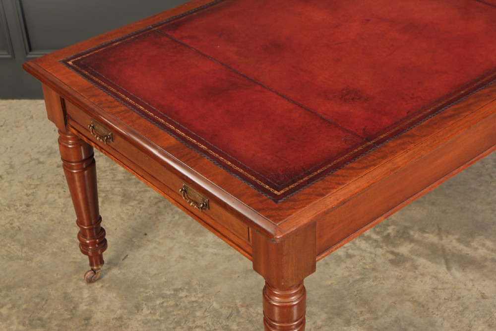 A Victorian mahogany writing table with a red leather inset surface, turned legs, and brass castors. View X