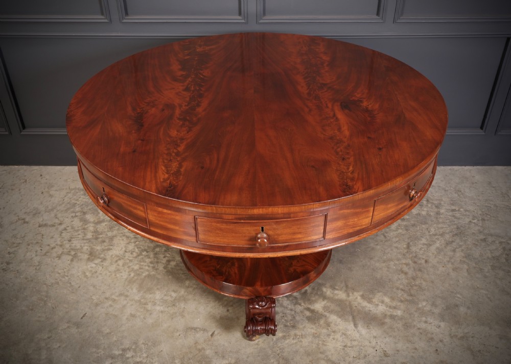 A circular William IV mahogany drum table featuring a flame mahogany top, frieze drawers with wooden knobs, a thick central column, and a circular plinth base with carved scroll feet. View II