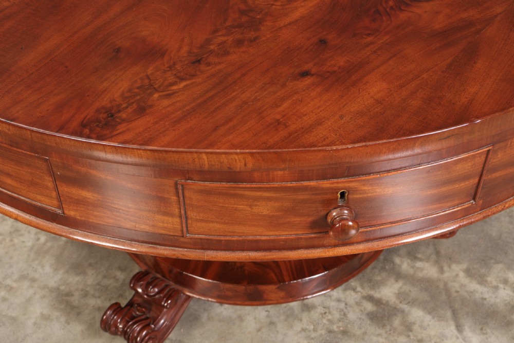 A circular William IV mahogany drum table featuring a flame mahogany top, frieze drawers with wooden knobs, a thick central column, and a circular plinth base with carved scroll feet. View V