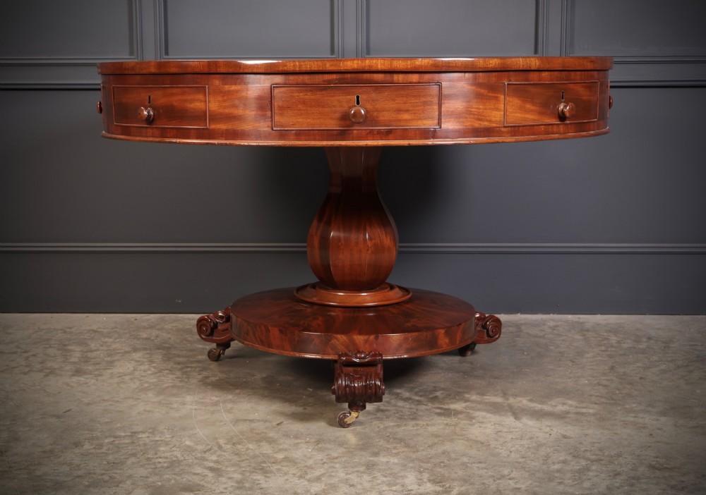 A circular William IV mahogany drum table featuring a flame mahogany top, frieze drawers with wooden knobs, a thick central column, and a circular plinth base with carved scroll feet. View VI