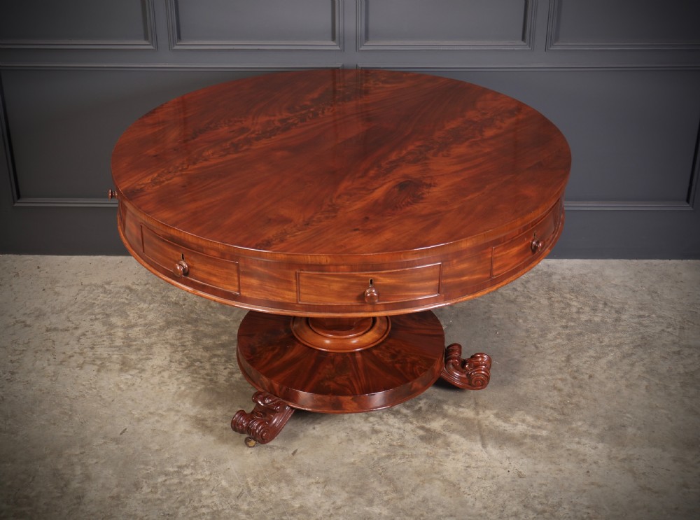 A circular William IV mahogany drum table featuring a flame mahogany top, frieze drawers with wooden knobs, a thick central column, and a circular plinth base with carved scroll feet. View VII