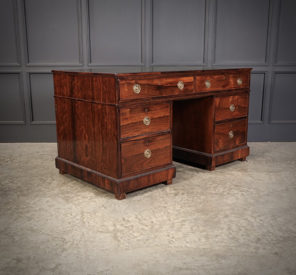 A William IV rosewood pedestal desk featuring a green leather writing surface, multiple drawers with brass ring handles, and decorative moulding around the lower base. View VII
