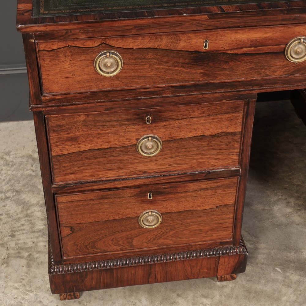 A William IV rosewood pedestal desk featuring a green leather writing surface, multiple drawers with brass ring handles, and decorative moulding around the lower base. View II