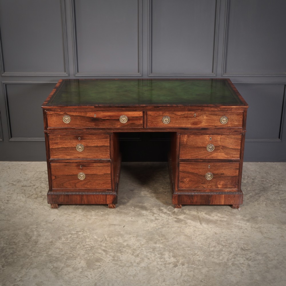A William IV rosewood pedestal desk featuring a green leather writing surface, multiple drawers with brass ring handles, and decorative moulding around the lower base. View III