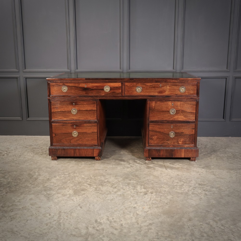 A William IV rosewood pedestal desk featuring a green leather writing surface, multiple drawers with brass ring handles, and decorative moulding around the lower base. View V