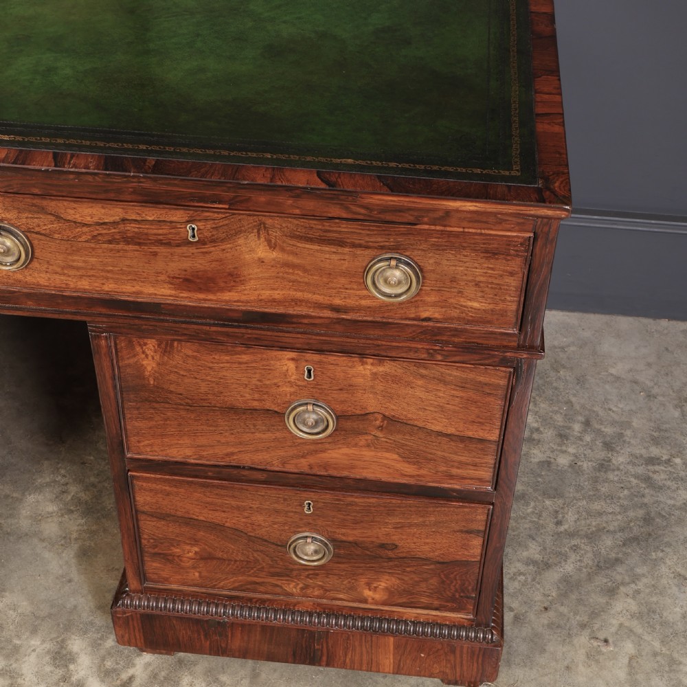 A William IV rosewood pedestal desk featuring a green leather writing surface, multiple drawers with brass ring handles, and decorative moulding around the lower base. View VI