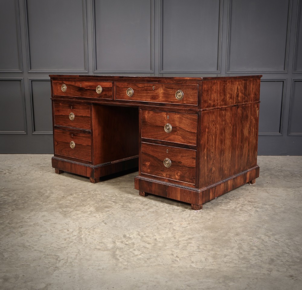 A William IV rosewood pedestal desk featuring a green leather writing surface, multiple drawers with brass ring handles, and decorative moulding around the lower base. View VIII