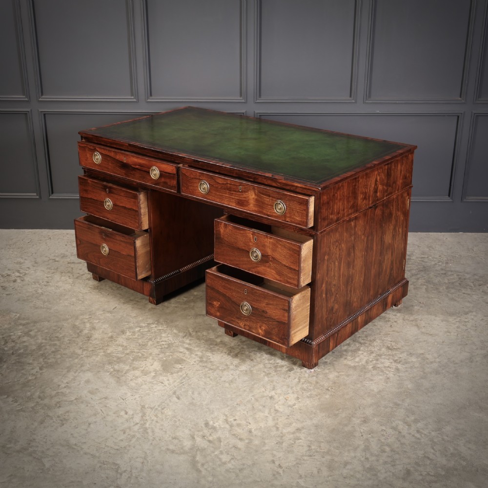 A William IV rosewood pedestal desk featuring a green leather writing surface, multiple drawers with brass ring handles, and decorative moulding around the lower base. View IX