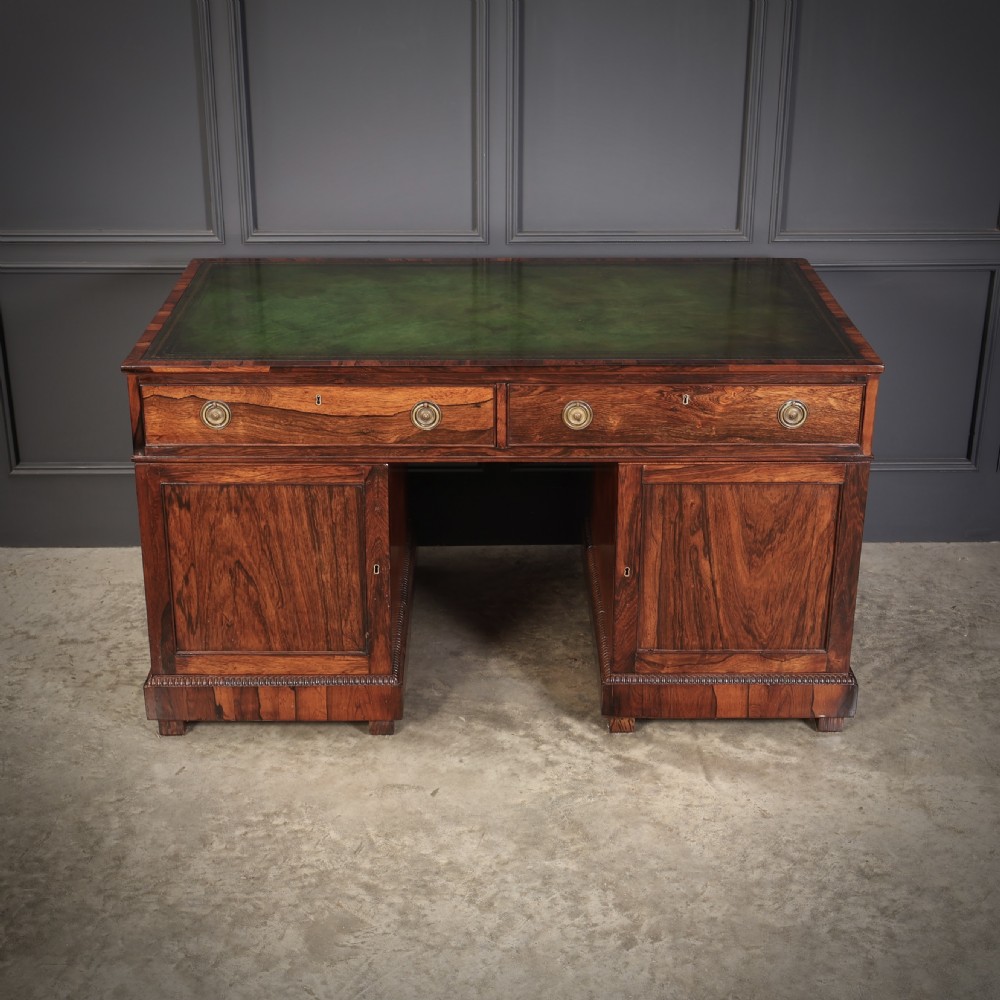 A William IV rosewood pedestal desk featuring a green leather writing surface, multiple drawers with brass ring handles, and decorative moulding around the lower base. View XI