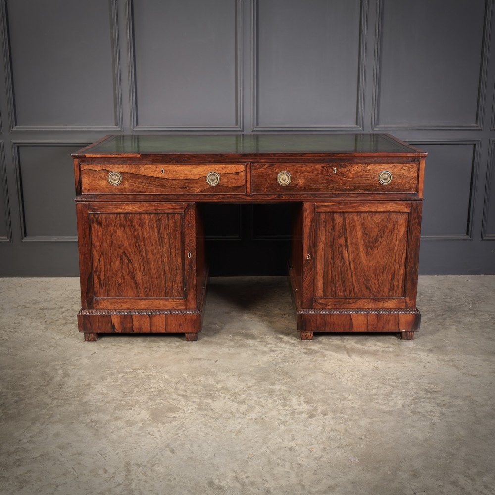 A William IV rosewood pedestal desk featuring a green leather writing surface, multiple drawers with brass ring handles, and decorative moulding around the lower base. View XII