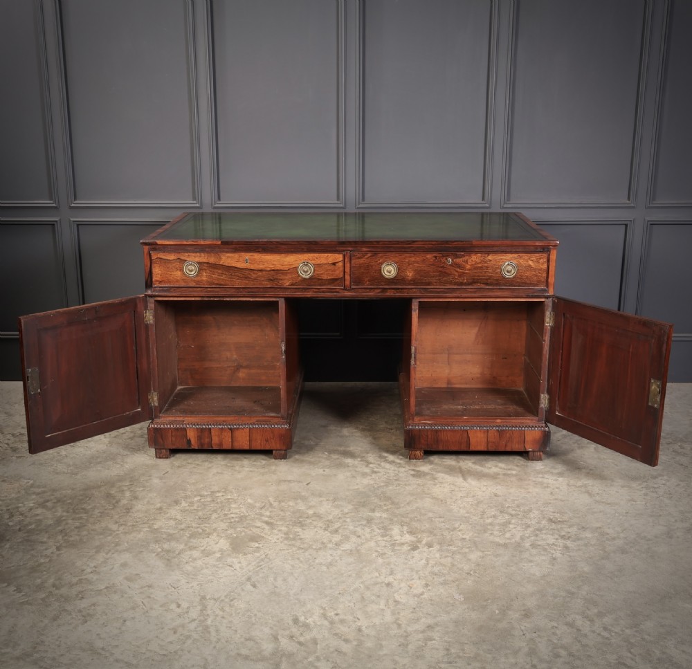 A William IV rosewood pedestal desk featuring a green leather writing surface, multiple drawers with brass ring handles, and decorative moulding around the lower base. View XIII