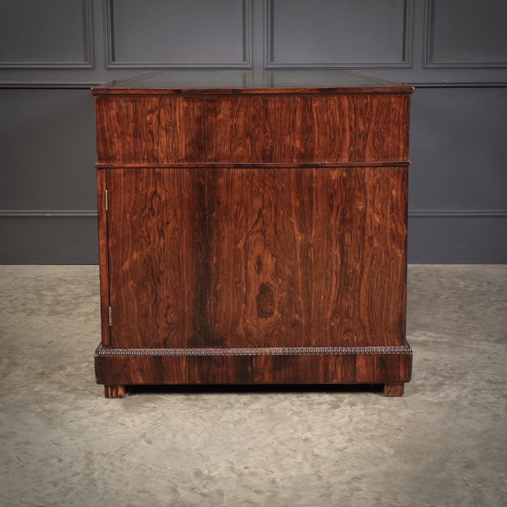 A William IV rosewood pedestal desk featuring a green leather writing surface, multiple drawers with brass ring handles, and decorative moulding around the lower base. View XIV