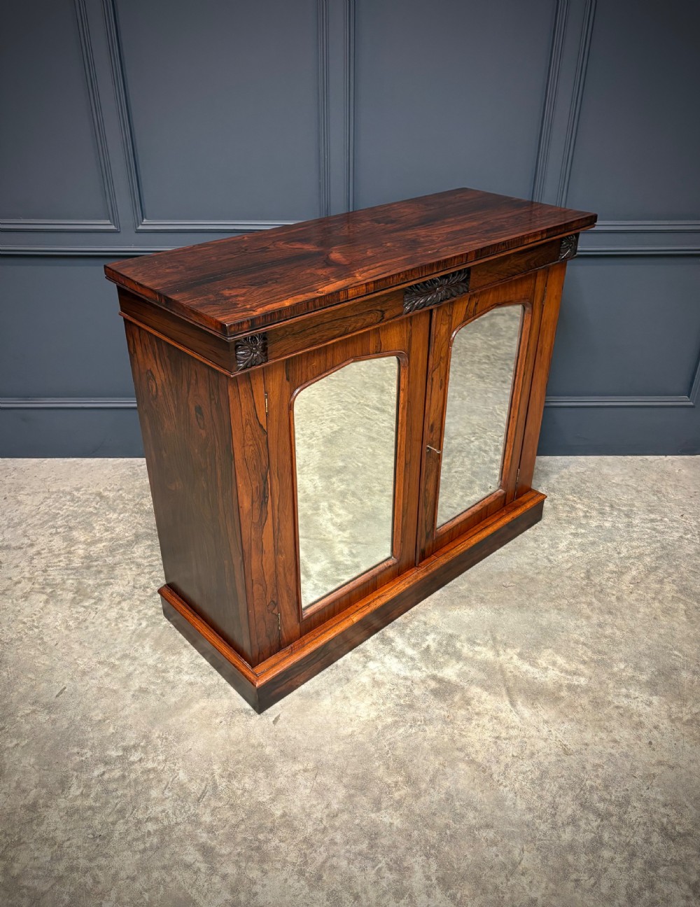 A William IV rosewood side cabinet with twin arch-topped mirrored doors, carved foliage details along the frieze, and a sturdy plinth base. View II