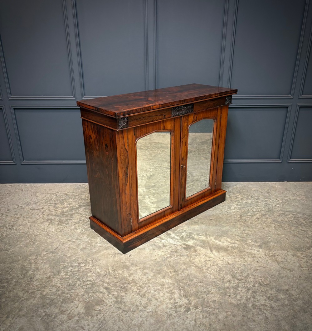 A William IV rosewood side cabinet with twin arch-topped mirrored doors, carved foliage details along the frieze, and a sturdy plinth base. View III