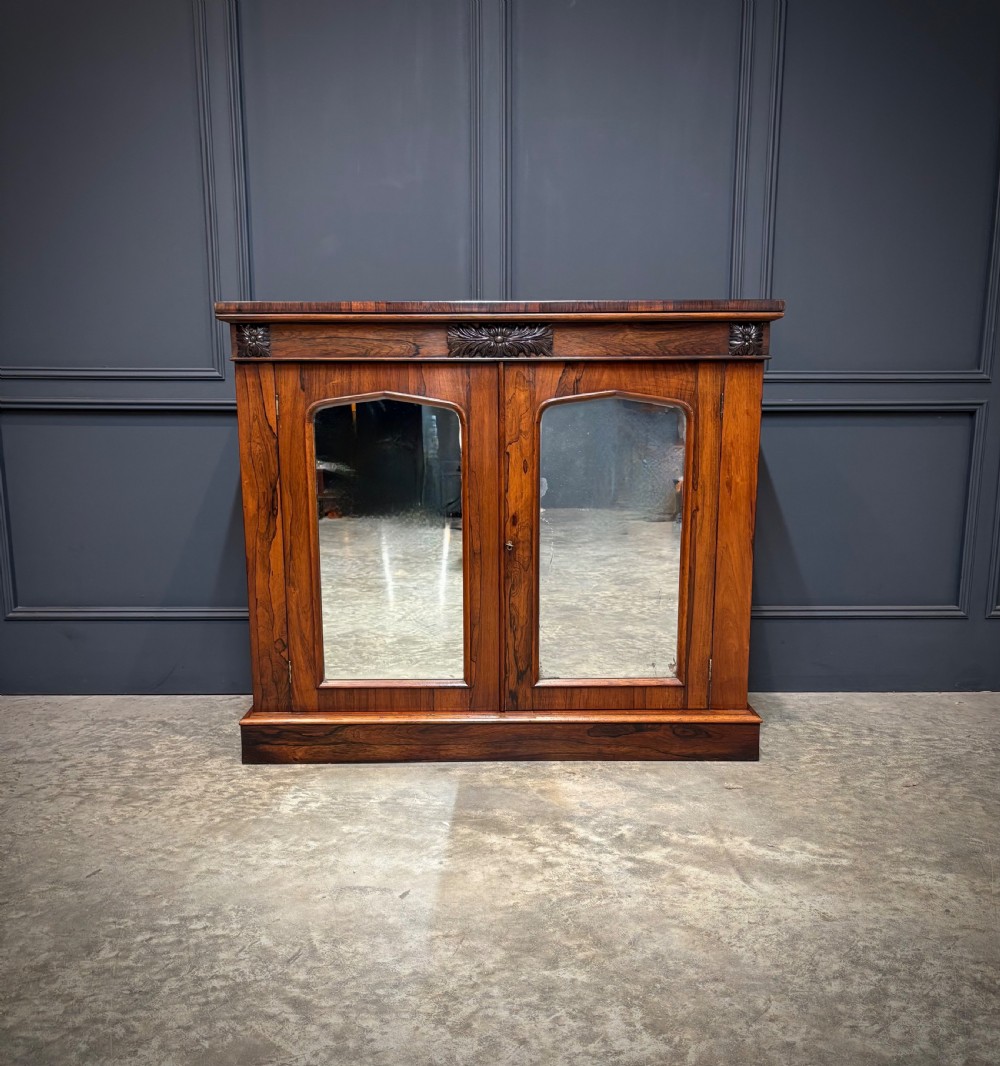 A William IV rosewood side cabinet with twin arch-topped mirrored doors, carved foliage details along the frieze, and a sturdy plinth base. View V