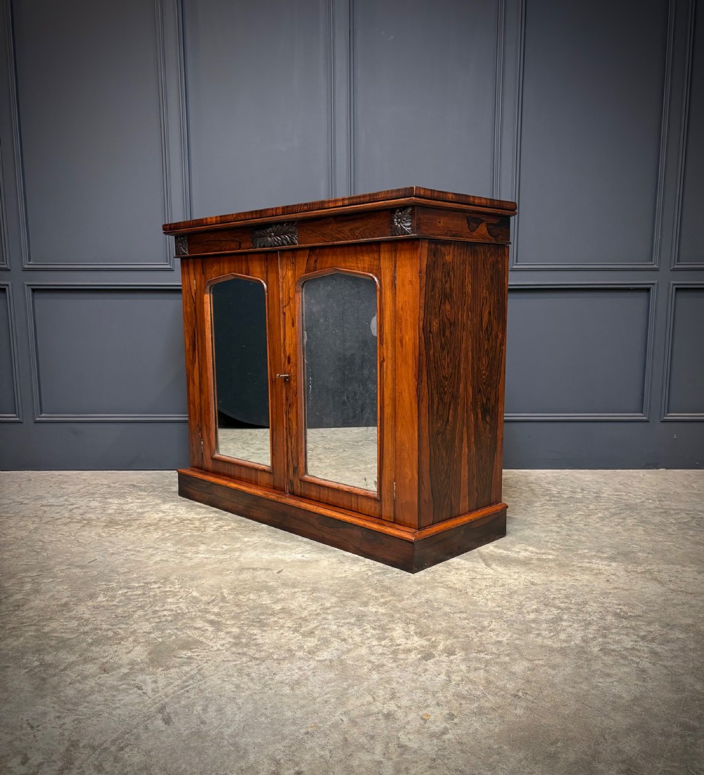 A William IV rosewood side cabinet with twin arch-topped mirrored doors, carved foliage details along the frieze, and a sturdy plinth base. View VII