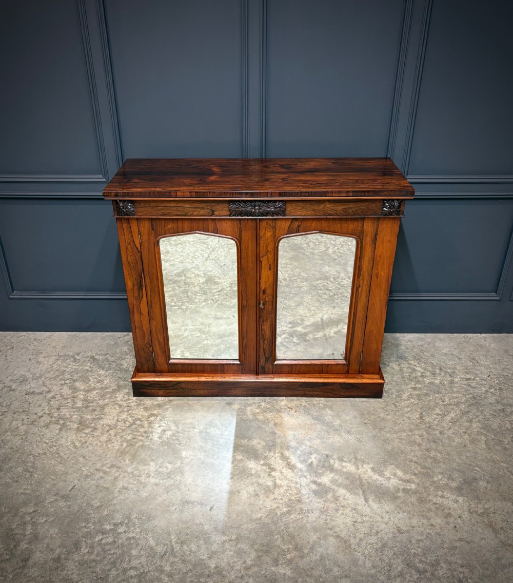 A William IV rosewood side cabinet with twin arch-topped mirrored doors, carved foliage details along the frieze, and a sturdy plinth base. View VIII