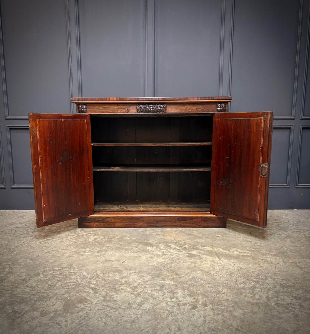 A William IV rosewood side cabinet with twin arch-topped mirrored doors, carved foliage details along the frieze, and a sturdy plinth base. View IX