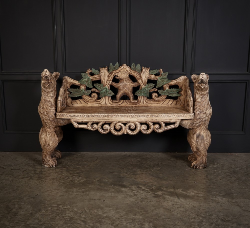 A carved light brown wooden two-seat bench featuring full-standing bear supports on each side and a central carved bear with green painted leaves on the backrest.