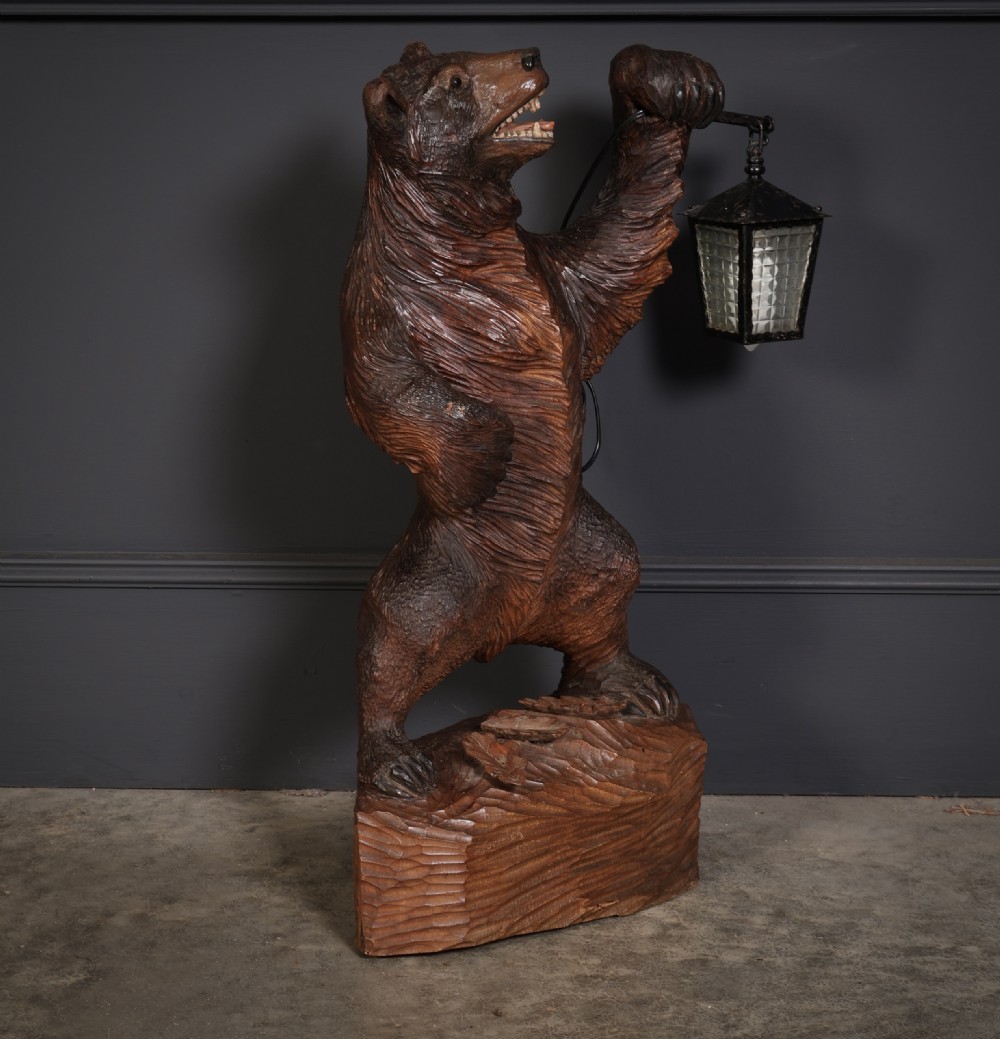A hand-carved wooden standing bear holding a metal lantern fixture on a carved timber base.