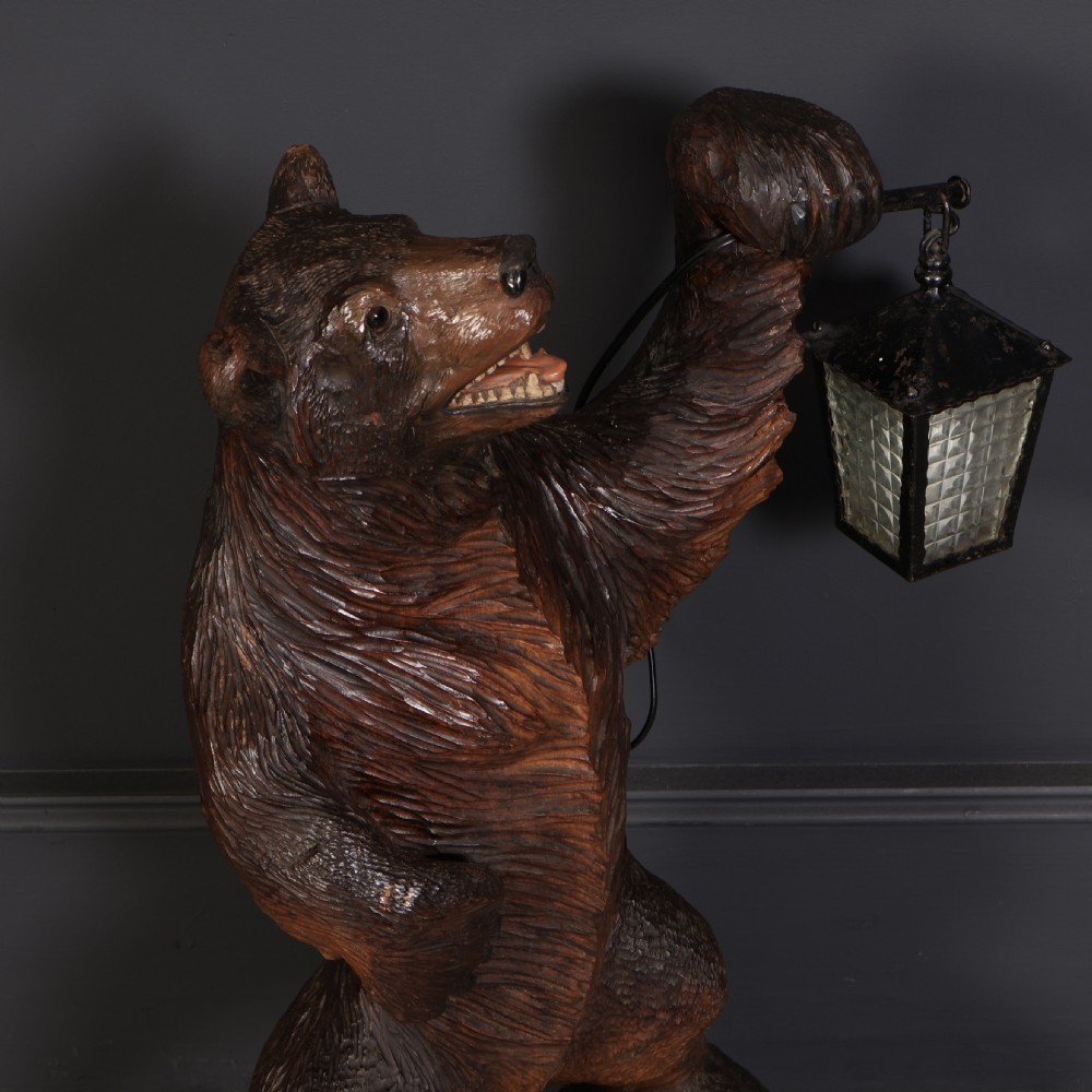 A hand-carved wooden standing bear holding a metal lantern fixture on a carved timber base. View II