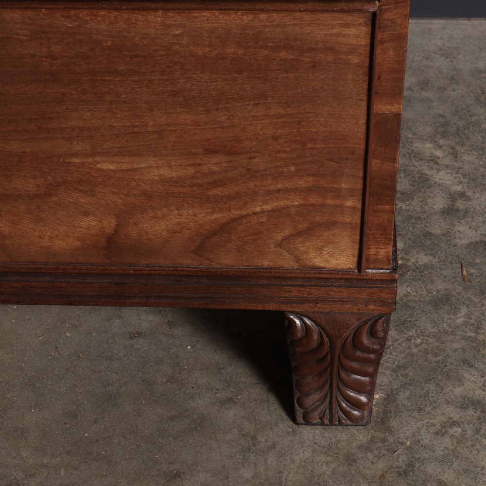 A late Regency mahogany linen press featuring a carved scrolled pediment, double panelled doors with flame mahogany veneers, and a base with four drawers. View VI