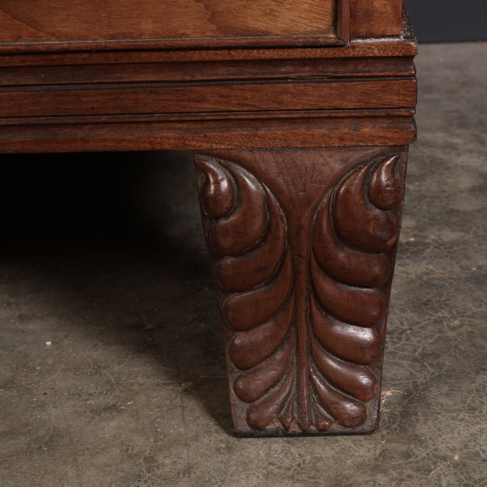A late Regency mahogany linen press featuring a carved scrolled pediment, double panelled doors with flame mahogany veneers, and a base with four drawers. View X