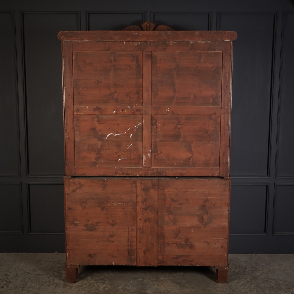 A late Regency mahogany linen press featuring a carved scrolled pediment, double panelled doors with flame mahogany veneers, and a base with four drawers. View XVI