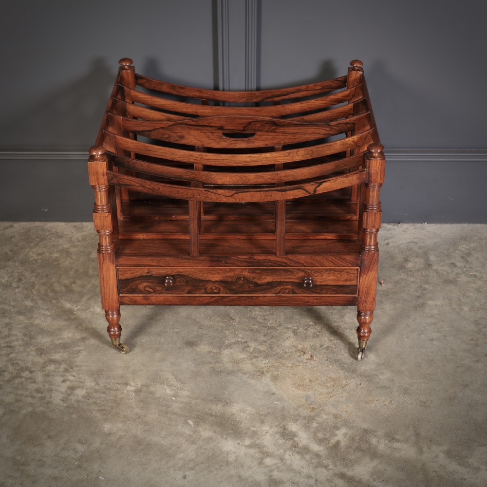 A Regency dark rosewood Canterbury music rack featuring concave slatted dividers, turned corner posts with finials, a lower drawer, and brass castors. View III