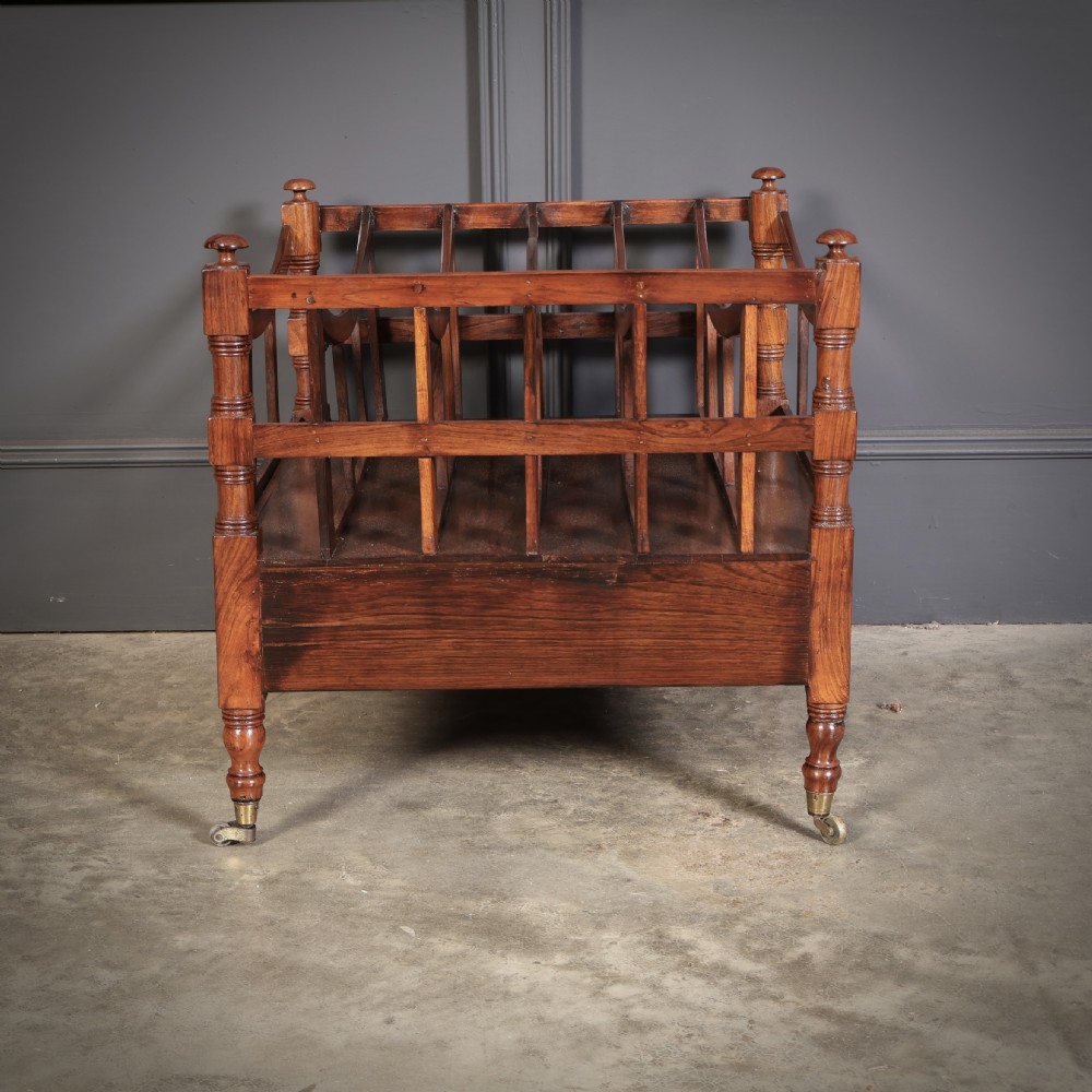 A Regency dark rosewood Canterbury music rack featuring concave slatted dividers, turned corner posts with finials, a lower drawer, and brass castors. View VIII