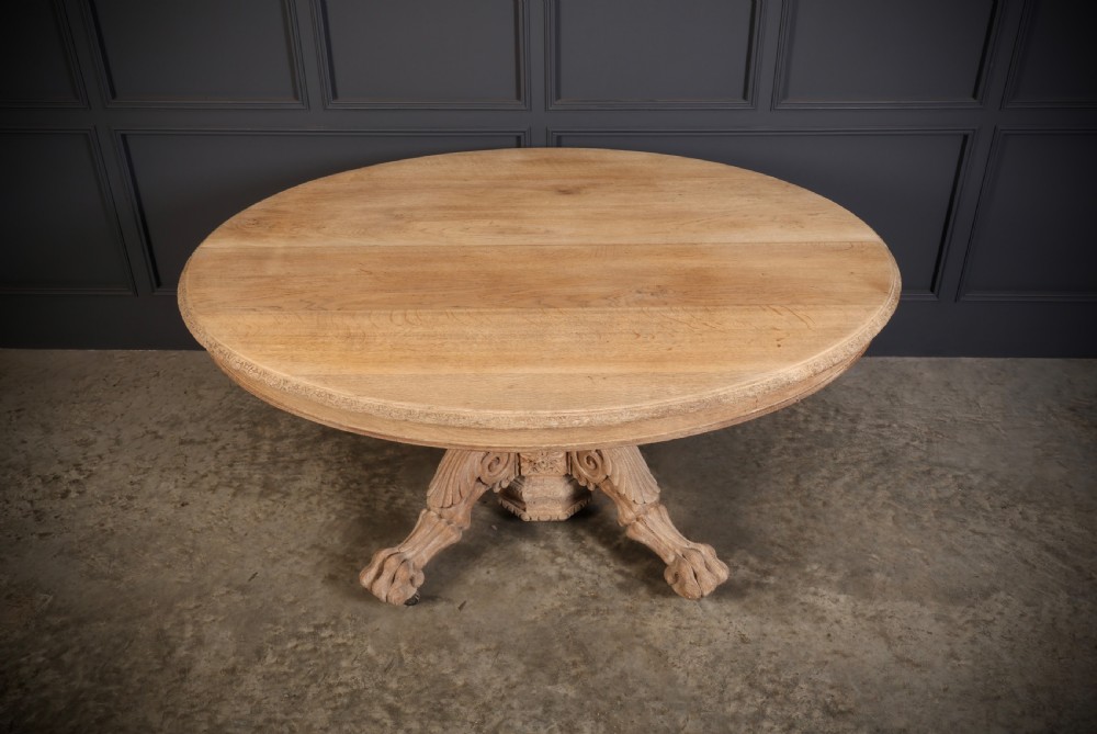 An oval bleached oak centre table featuring an intricately carved pedestal base with scroll legs and paw feet. View III