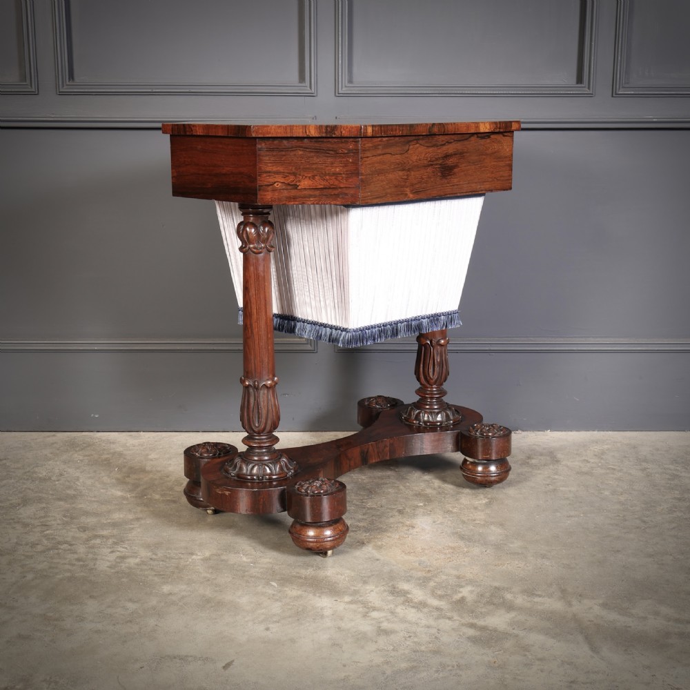 A William IV rosewood sewing table featuring an octagonal hinged top, a pleated fabric work basket, and carved twin column supports on a plinth base. View II