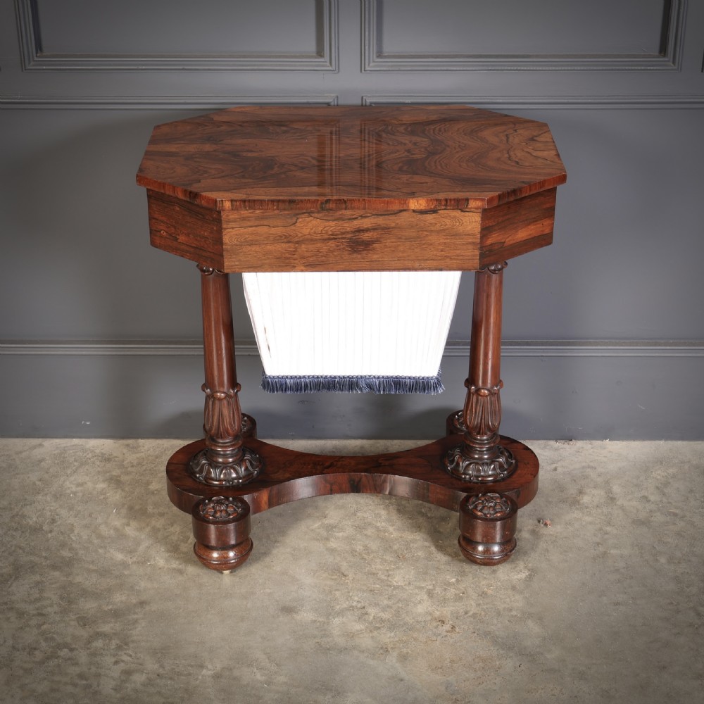 A William IV rosewood sewing table featuring an octagonal hinged top, a pleated fabric work basket, and carved twin column supports on a plinth base. View VI