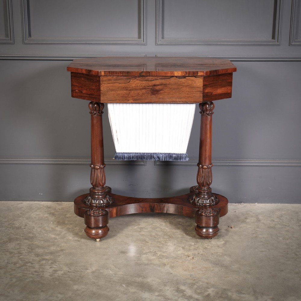 A William IV rosewood sewing table featuring an octagonal hinged top, a pleated fabric work basket, and carved twin column supports on a plinth base. View VII