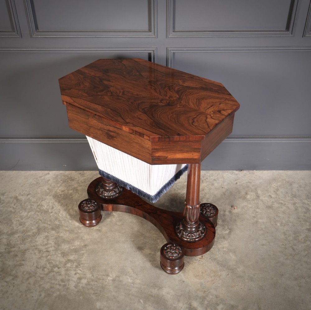 A William IV rosewood sewing table featuring an octagonal hinged top, a pleated fabric work basket, and carved twin column supports on a plinth base. View VIII
