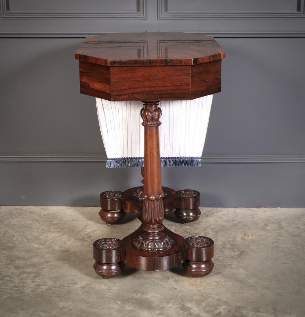 A William IV rosewood sewing table featuring an octagonal hinged top, a pleated fabric work basket, and carved twin column supports on a plinth base. View IX