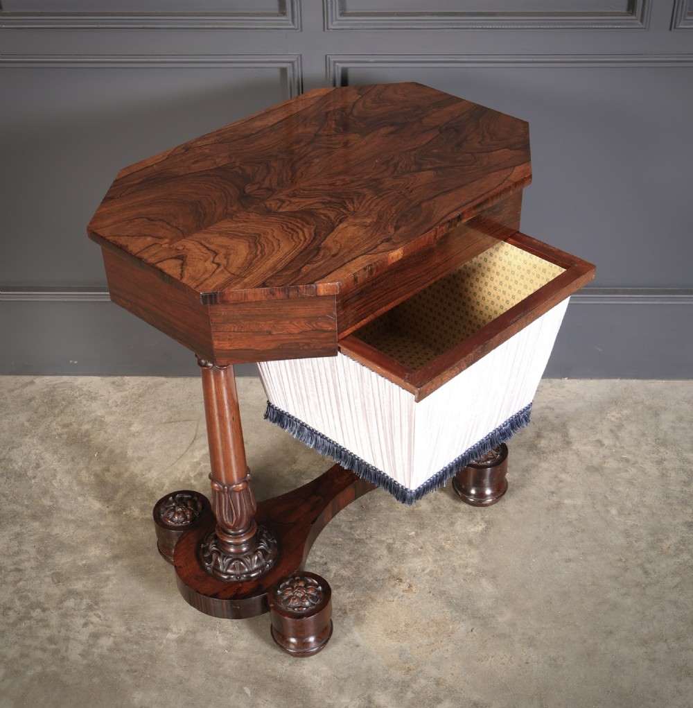 A William IV rosewood sewing table featuring an octagonal hinged top, a pleated fabric work basket, and carved twin column supports on a plinth base. View XI